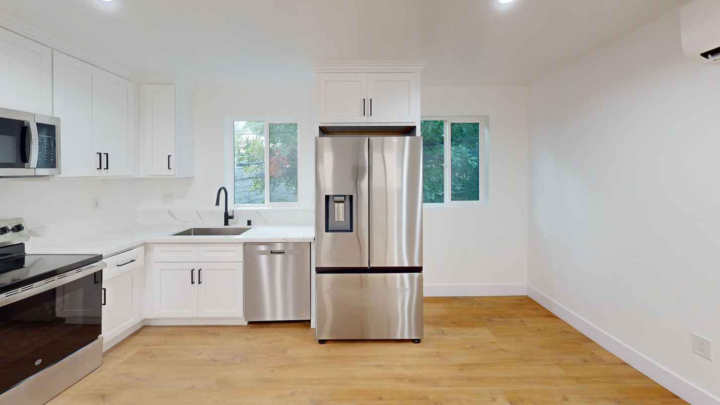 Modern kitchen with white cabinets, stainless steel appliances, and wood flooring.
