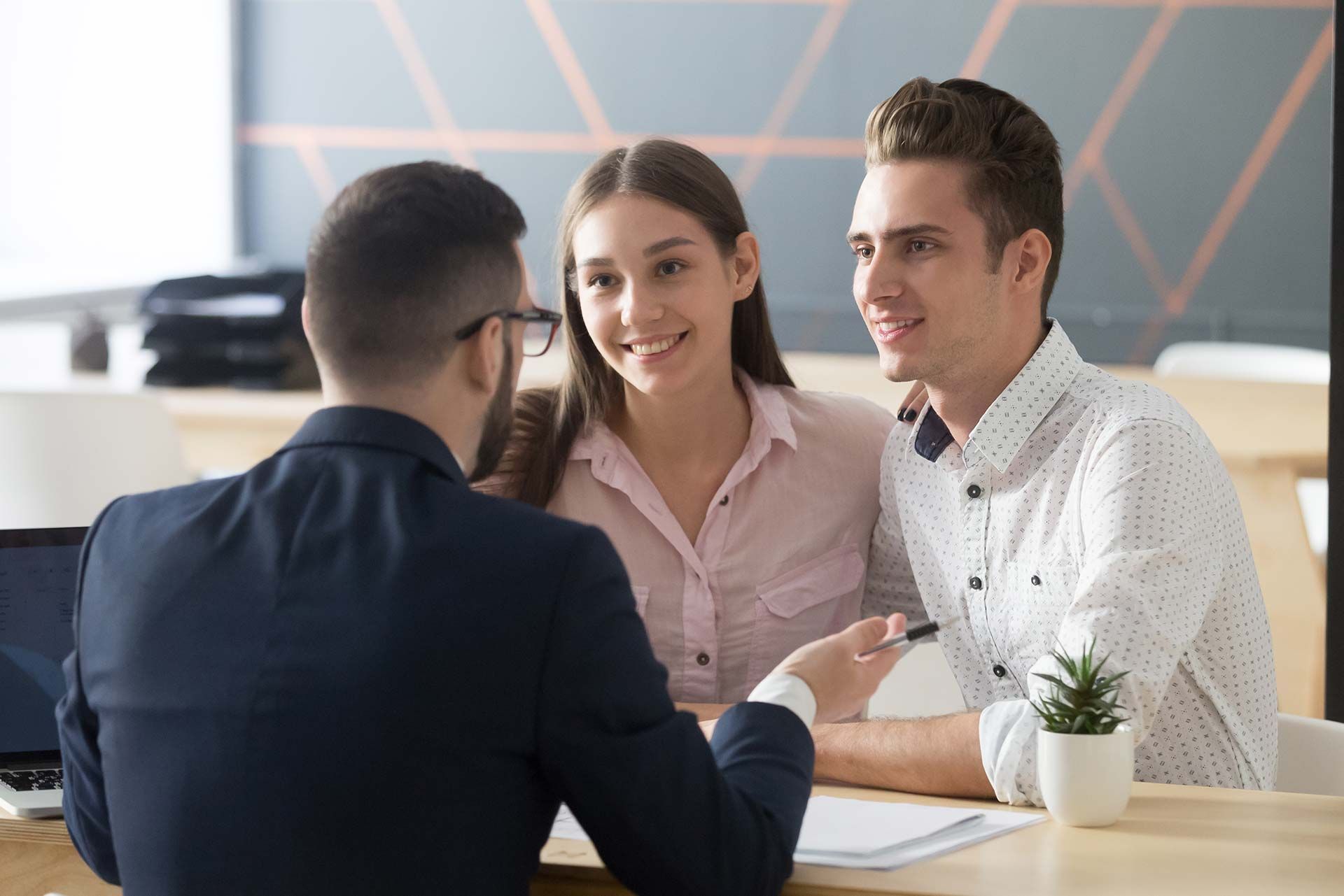 A couple smiles while meeting with a professional at a desk.
