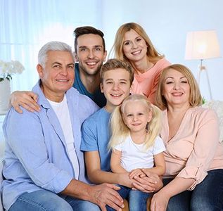 Family portrait: Six people, smiling, posing together indoors on a couch.