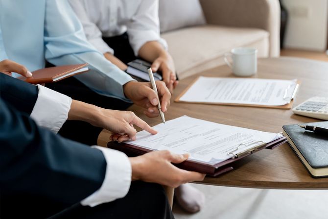 People reviewing documents and signing a paper at a table. A pen is in use.