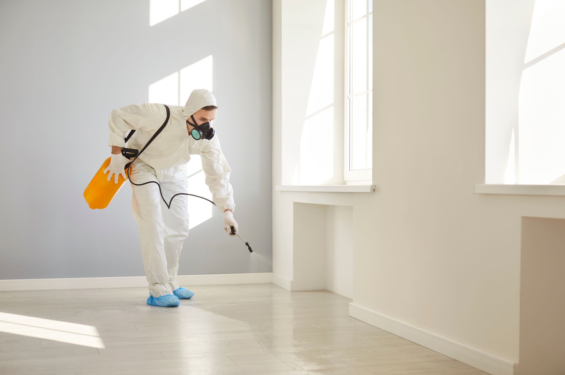 Pest control worker in protective suit spraying a room. Pest control worker in protective suit spraying a room.