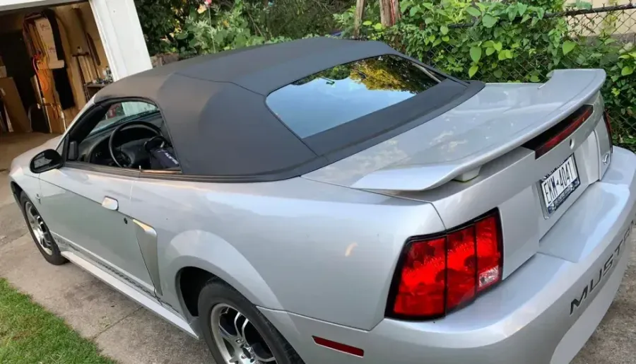 A silver mustang convertible is parked in front of a garage.