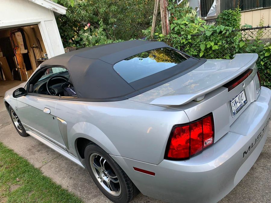 A silver mustang convertible is parked in front of a garage.