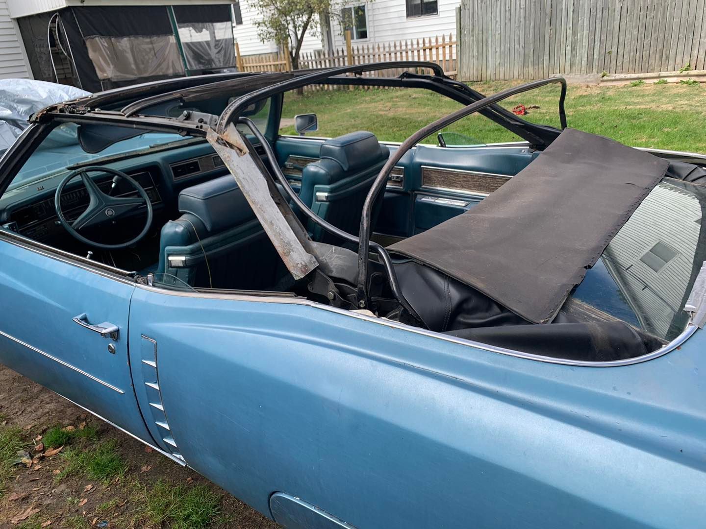 A blue convertible with the top down is parked in a yard.