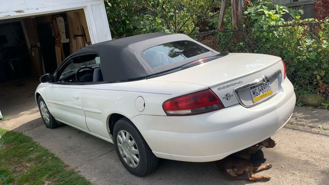 A white convertible car is parked in front of a garage.