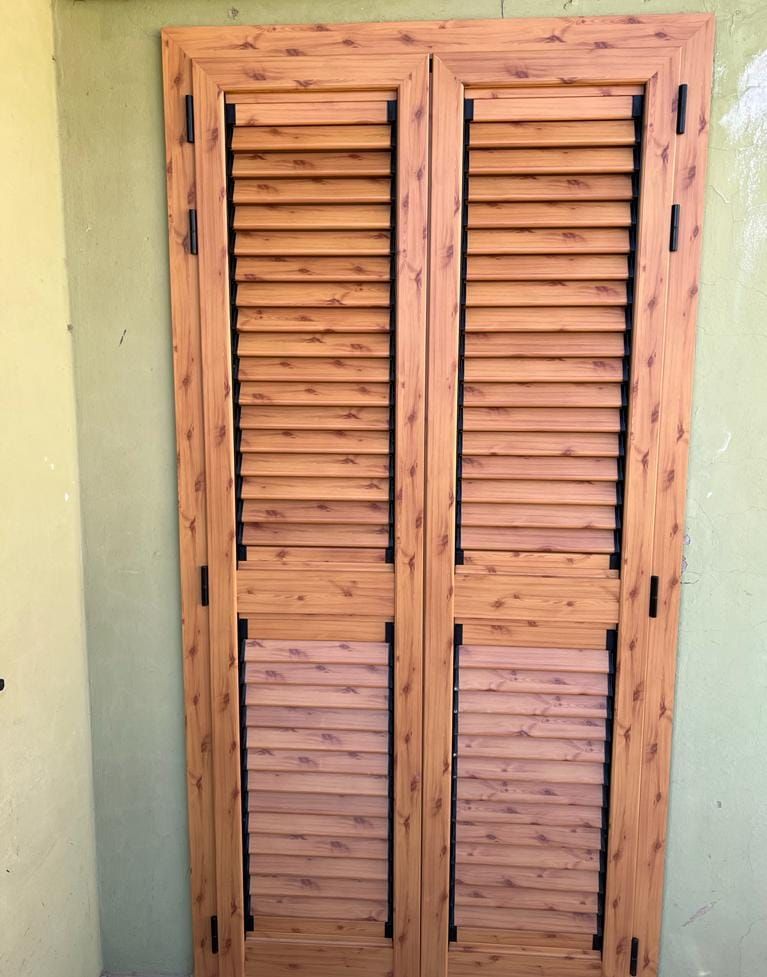 Una coppia di persiane a lamelle color legno chiaro stagliate su una parete semplice di colore verde chiaro.