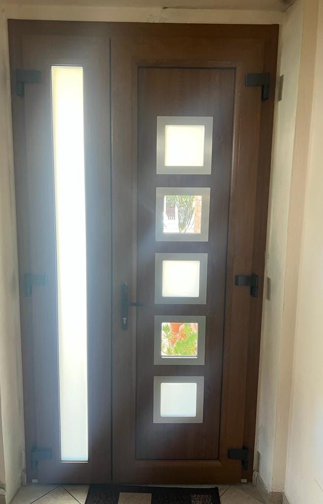Una porta d'ingresso marrone con un'alta e stretta anta di vetro smerigliato sulla sinistra e cinque piccole finestre quadrate smerigliate sulla destra.