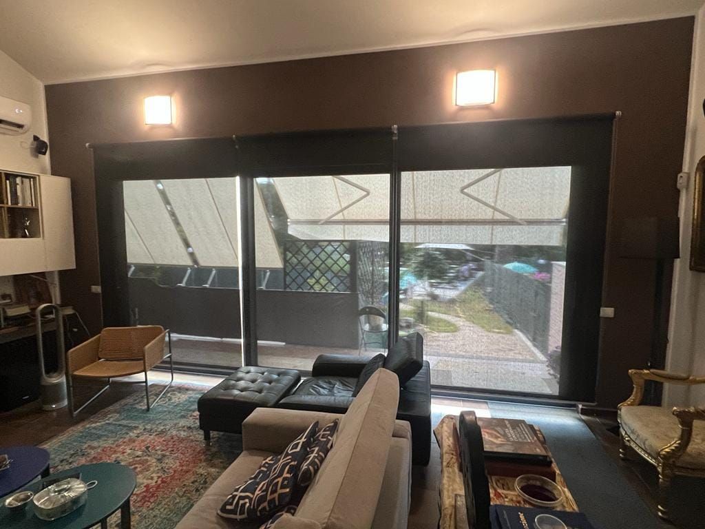 Un soggiorno moderno con ampie porte scorrevoli in vetro, mobili dai colori neutri, un tappeto a motivi geometrici e luci a parete dai toni caldi.