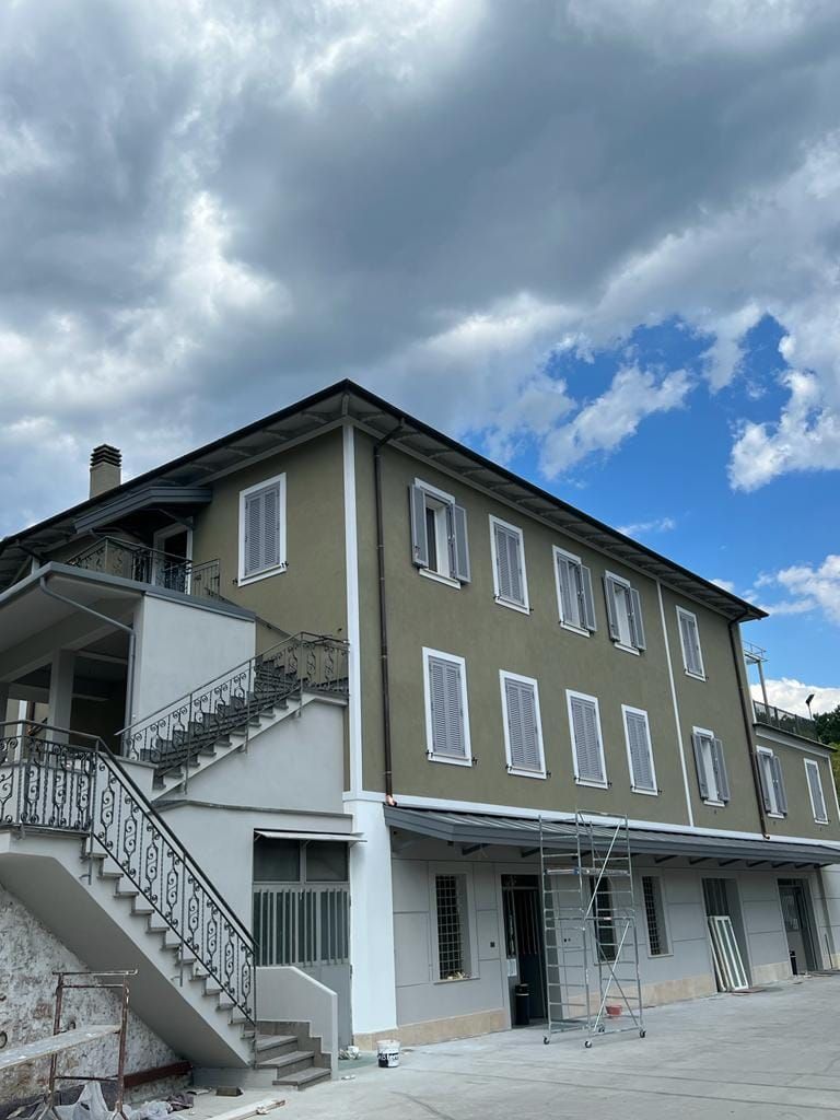 Un edificio a più piani con un piano terra di colore chiaro, un piano superiore verde oliva e una scala esterna a cielo aperto.