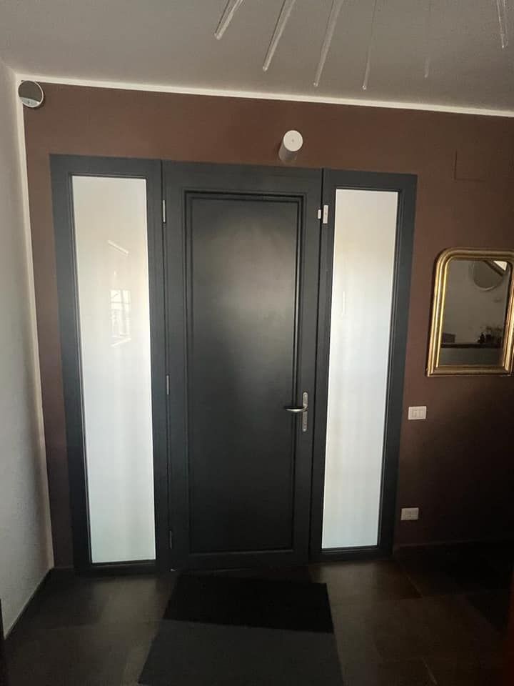 Un corridoio color marrone scuro con una moderna porta d'ingresso nera affiancata da due pannelli di vetro satinato e uno specchio a parete con cornice.