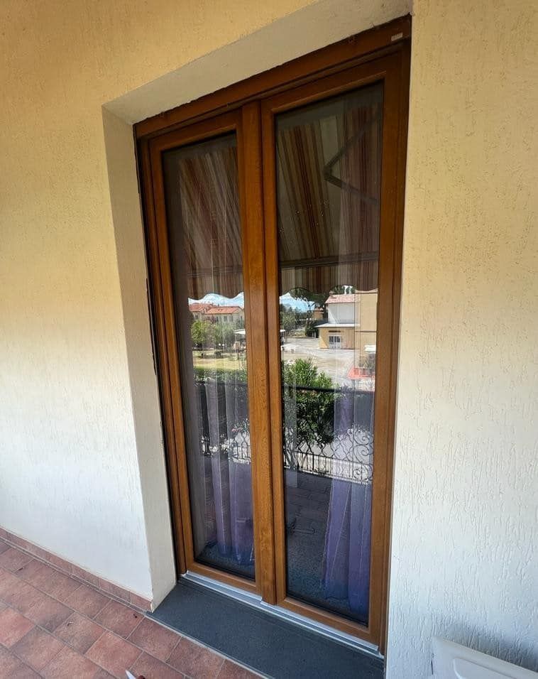 Una doppia porta a vetri con cornice marrone su un balcone, che offre uno scorcio del quartiere attraverso il vetro riflettente.