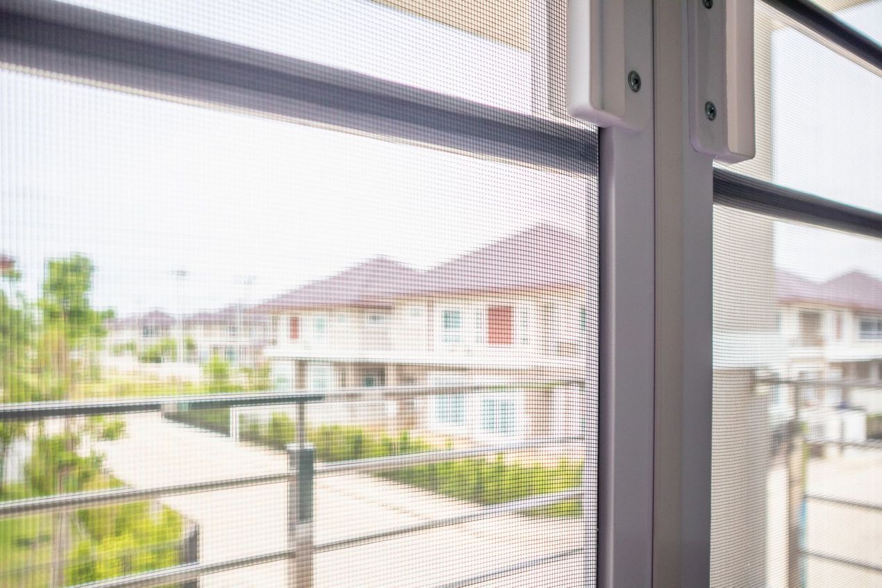 Una vista attraverso una zanzariera con cornice bianca che si affaccia su un quartiere residenziale con case di periferia.