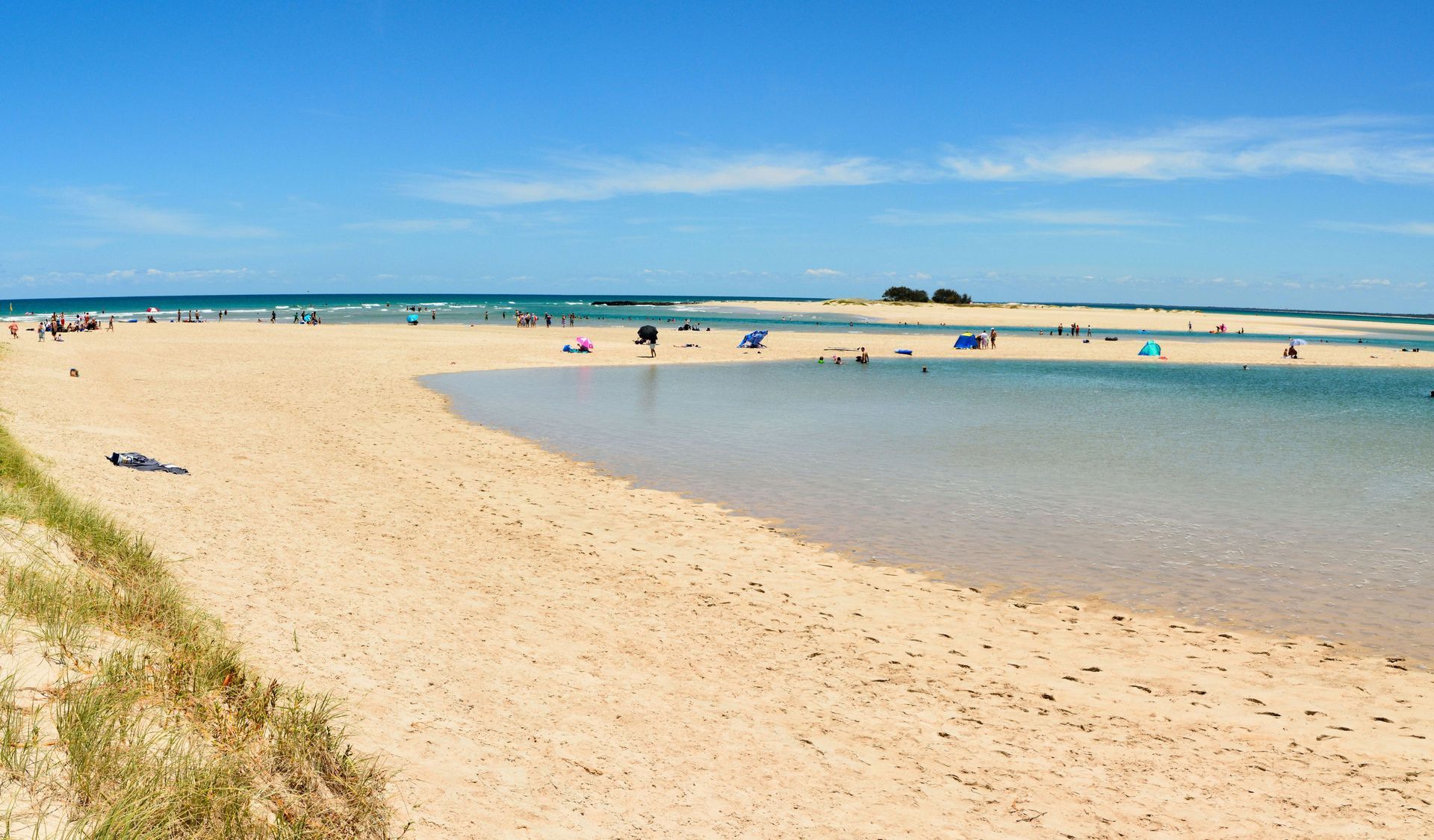 Sandy beach with calm water, people relaxing. Blue sky, distant islands.