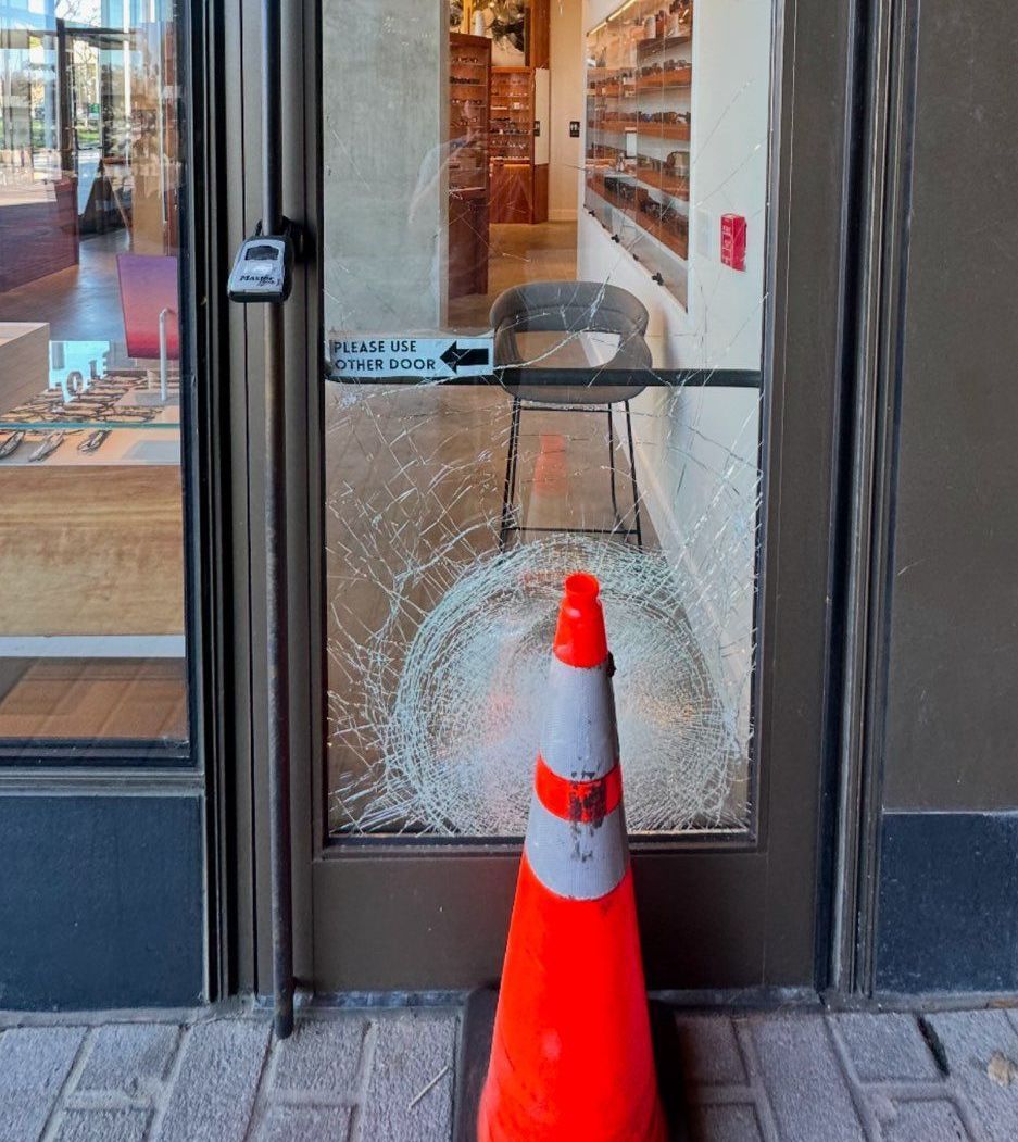 A broken glass door with a traffic cone in front of it