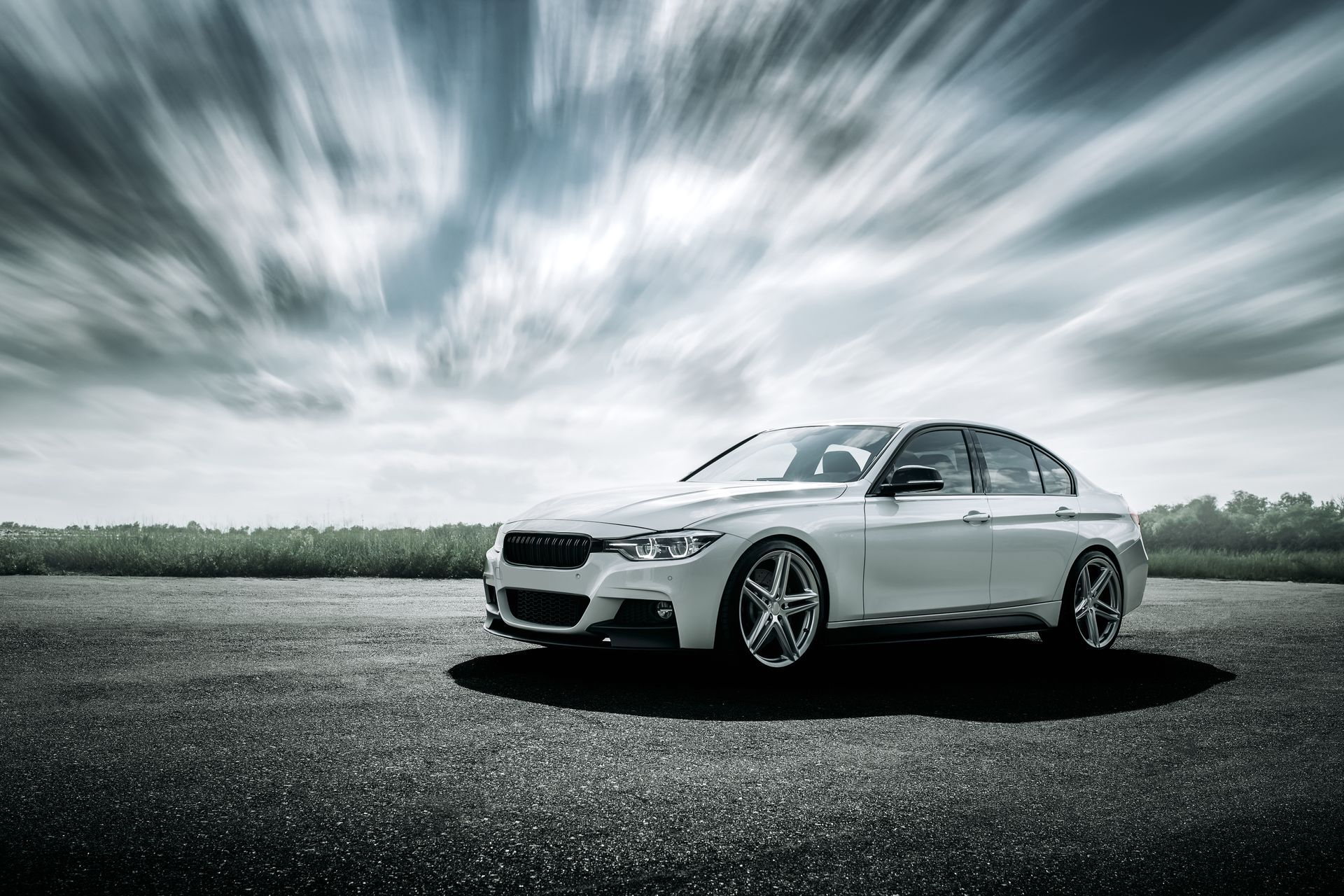 A white BMW sedan parked on an asphalt lot under a dramatic, streaky cloudy sky.