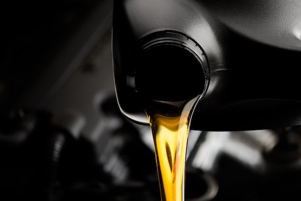 A black plastic container pouring golden motor oil into an engine.
