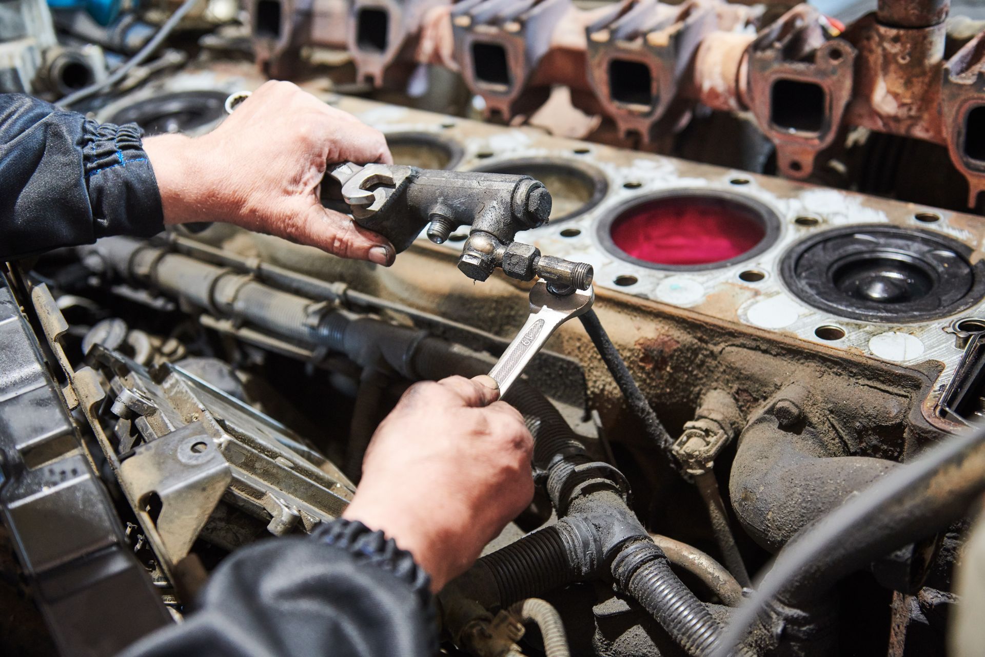 A person's hands use a wrench to repair a large, dirty engine block with visible internal cylinders.