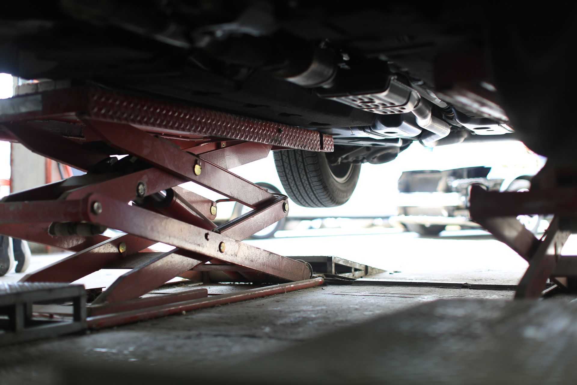 A low-angle view shows the underside of a car raised by a red hydraulic scissor lift in a garage.