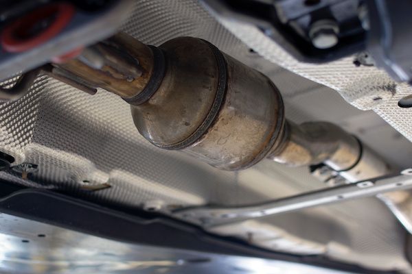 A close-up view of a car's metallic catalytic converter installed in the vehicle's undercarriage exhaust system.