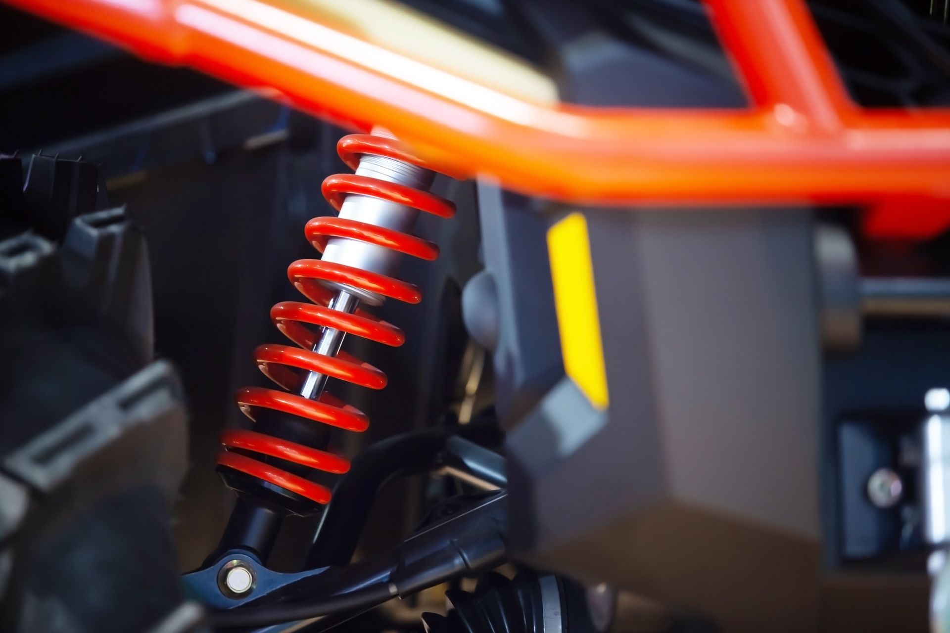 A close-up of a red coiled suspension spring on an off-road vehicle with an orange frame.