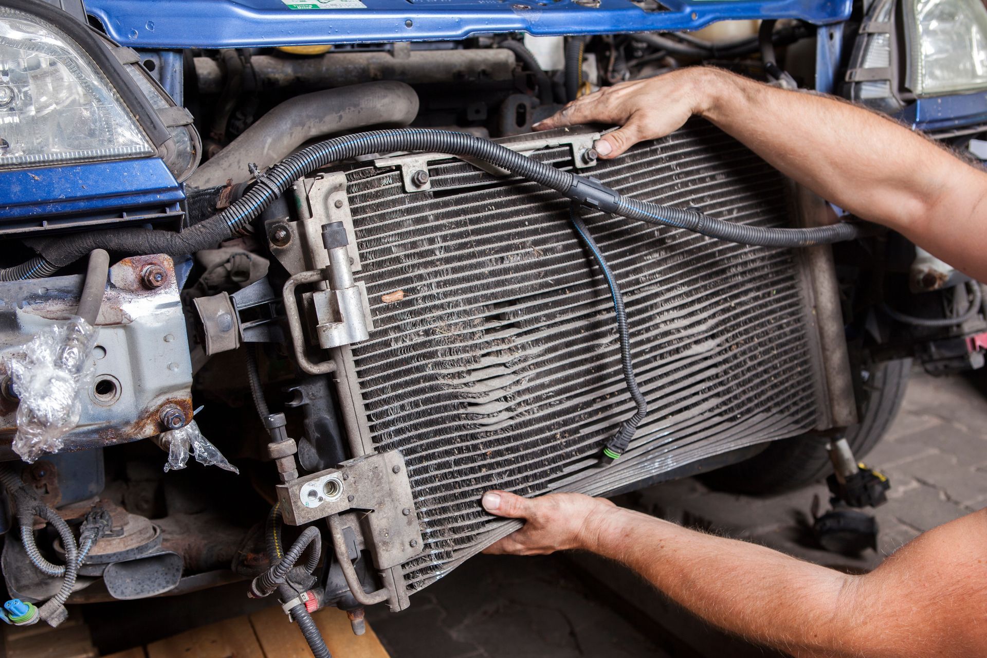 A mechanic holding a vehicle's radiator while performing repairs on the car's engine bay.