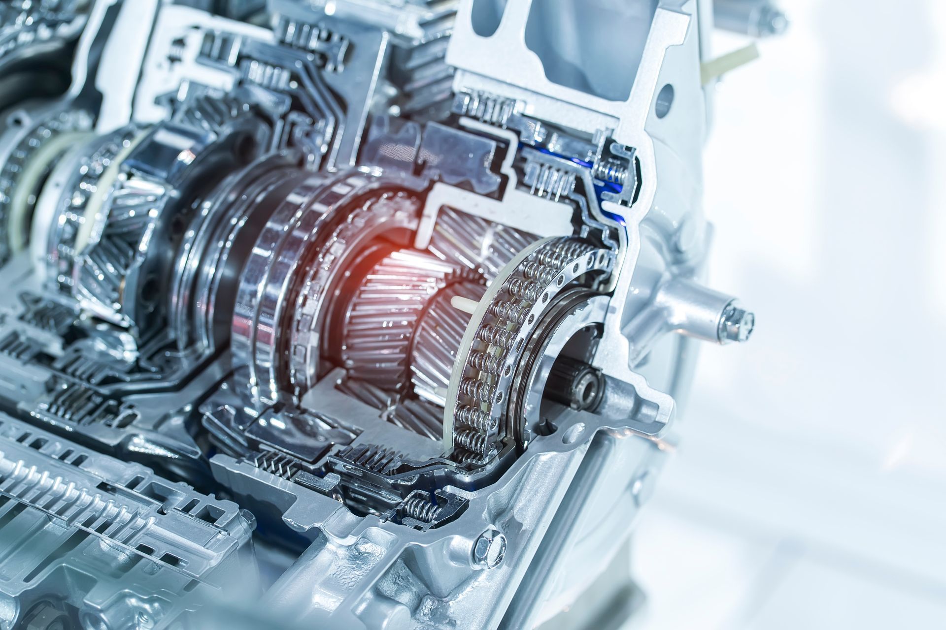 A close-up, cutaway view of a metallic vehicle transmission with gears highlighted by an orange glow.