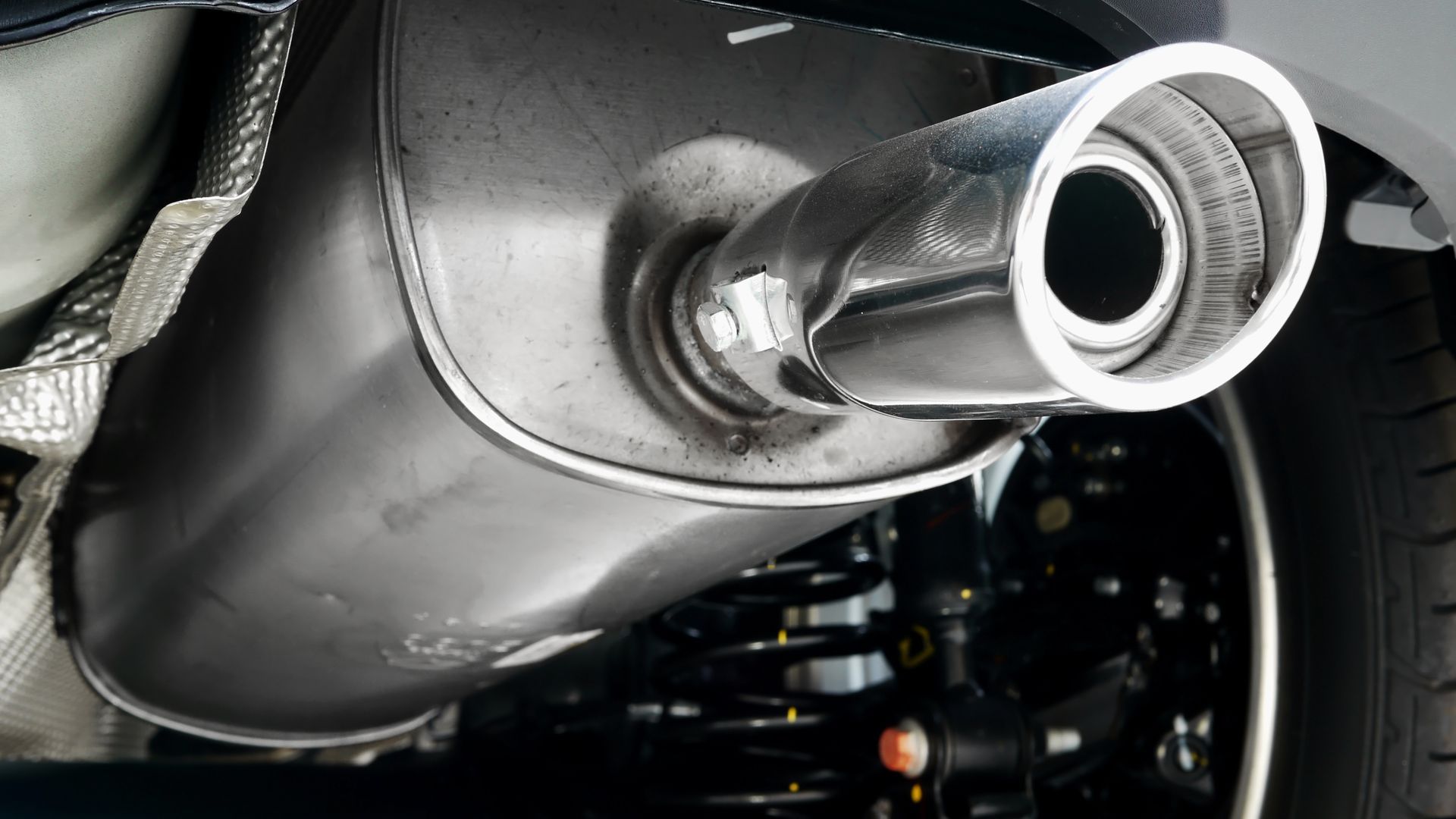 A close-up, underside view of a vehicle's metal exhaust muffler and chrome tailpipe assembly.