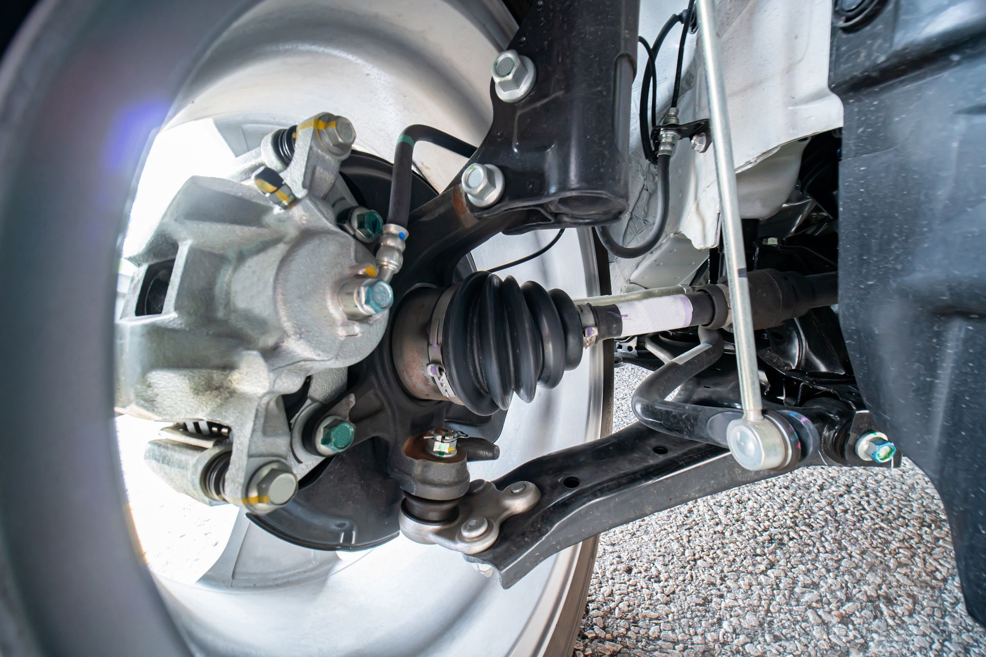Close-up view of an automobile's front suspension, showing the brake caliper, CV axle, and control arm.