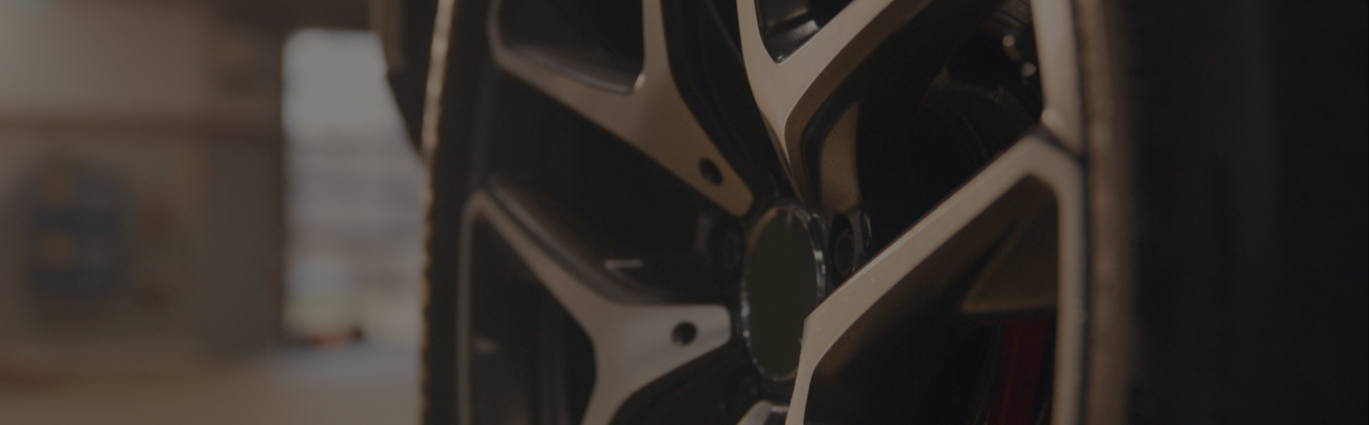 Close-up view of a metallic, geometric car rim with silver and black spokes, set against a softly blurred background.