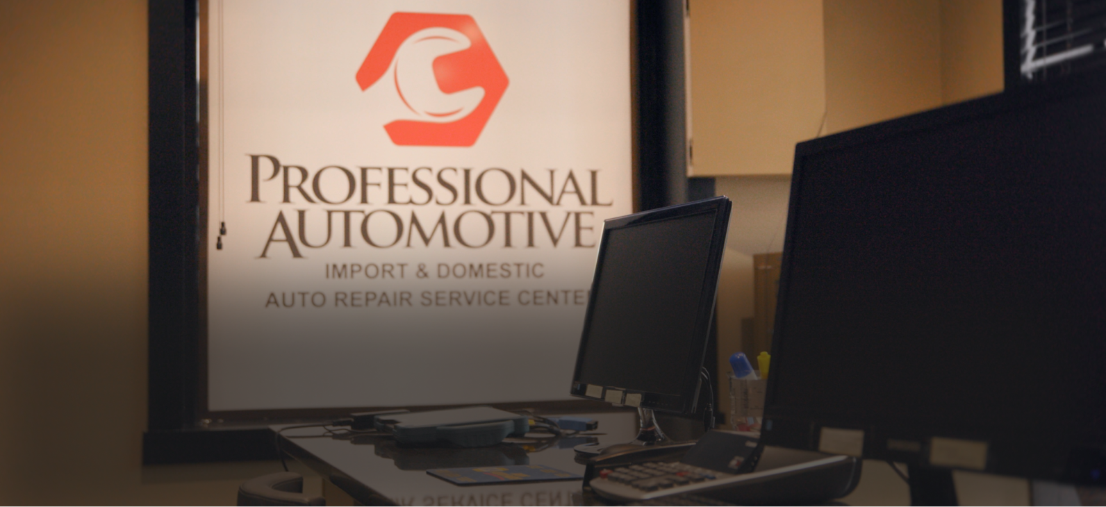 A Professional Automotive service center sign behind a desk with computer monitors in an office setting.
