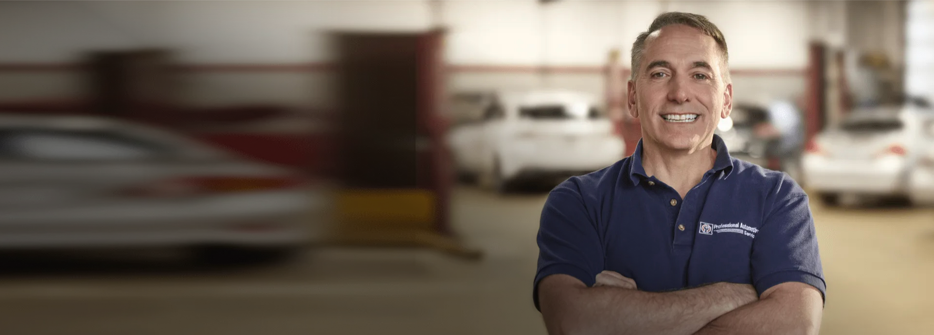 A person smiling in a blue polo shirt with a company logo, standing in front of a brick building with windows.