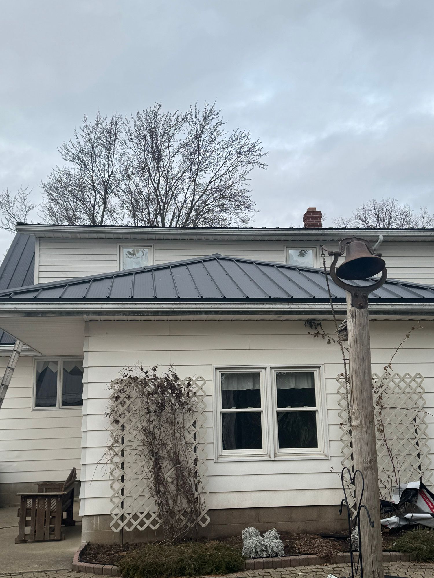 A white house with a black roof and a bell on the side of it.