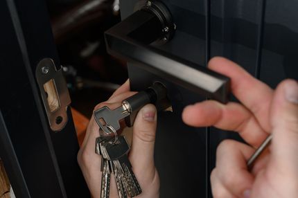 Hands installing a door handle, holding keys and a screwdriver