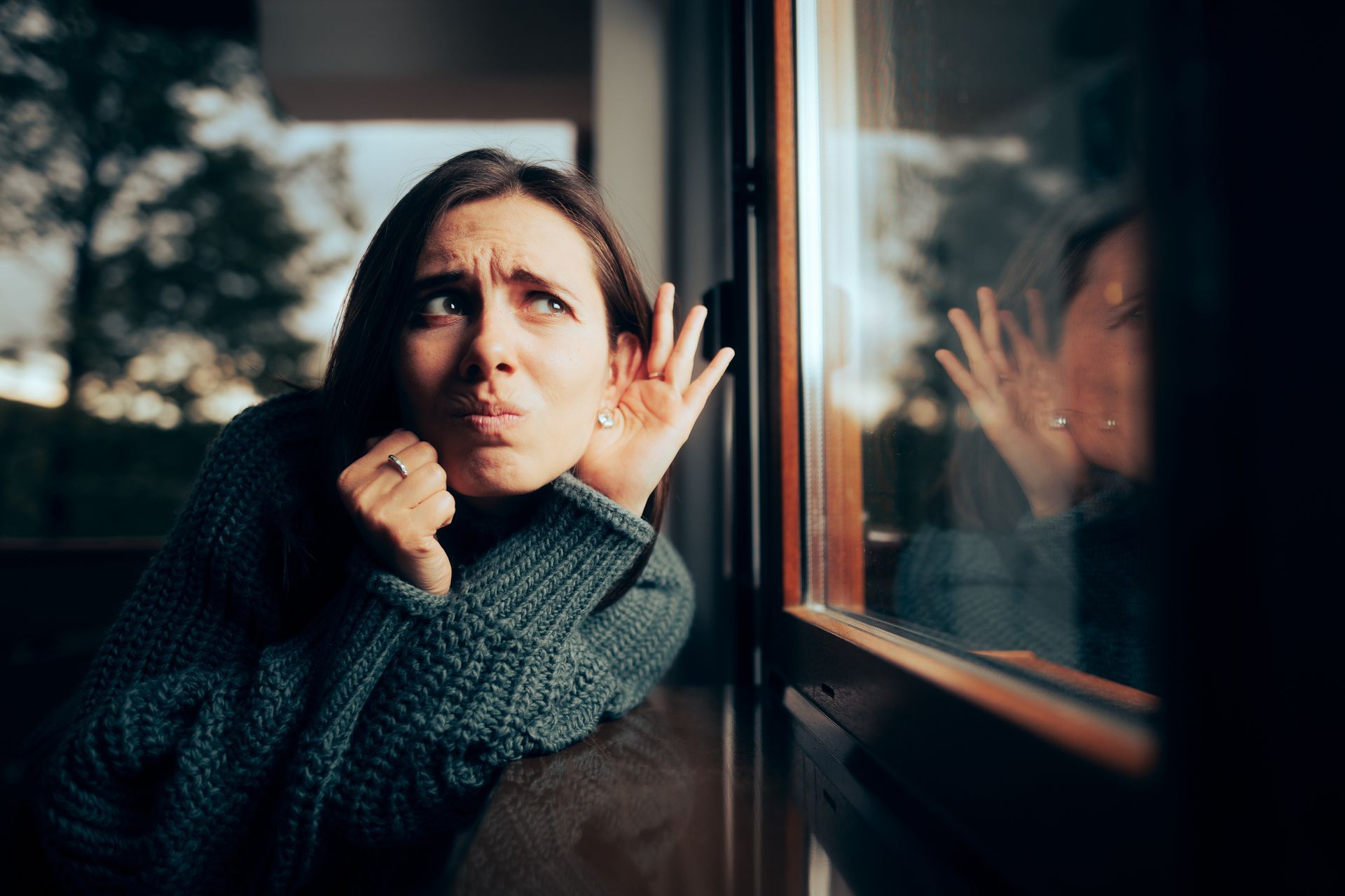 a woman is looking out of a window with her hand on her face listening to outdoor noise