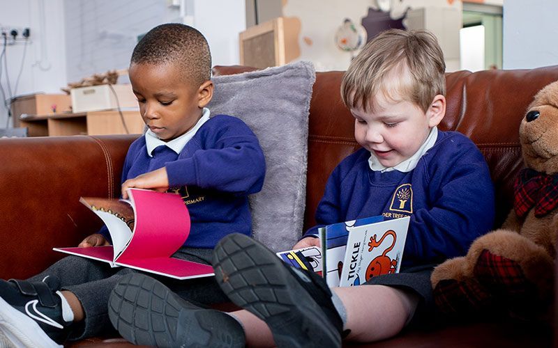 Two young boys are sitting on a couch reading books.