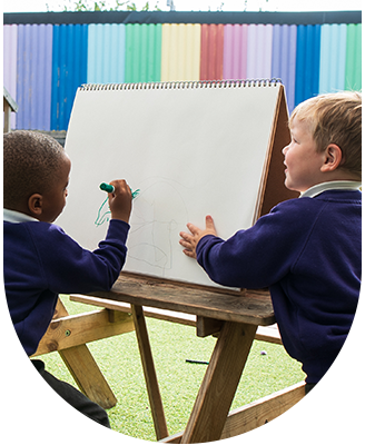 Two young boys are sitting at an easel drawing on a piece of paper.