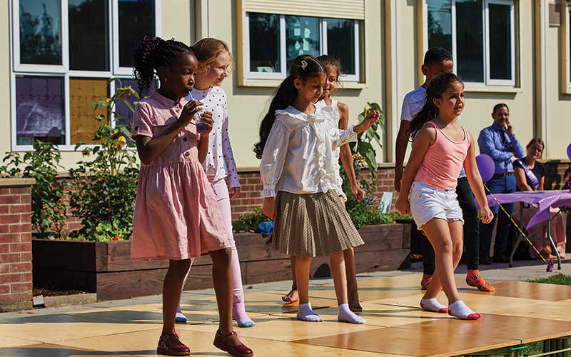 A group of young girls are dancing on a stage in front of a building.