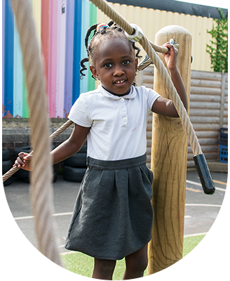 A little girl is standing next to a wooden post holding a rope.