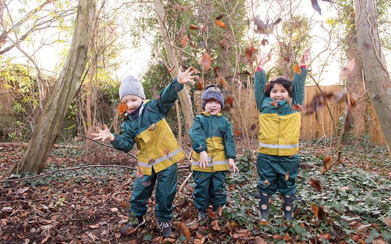 Three children are playing with leaves in the woods.