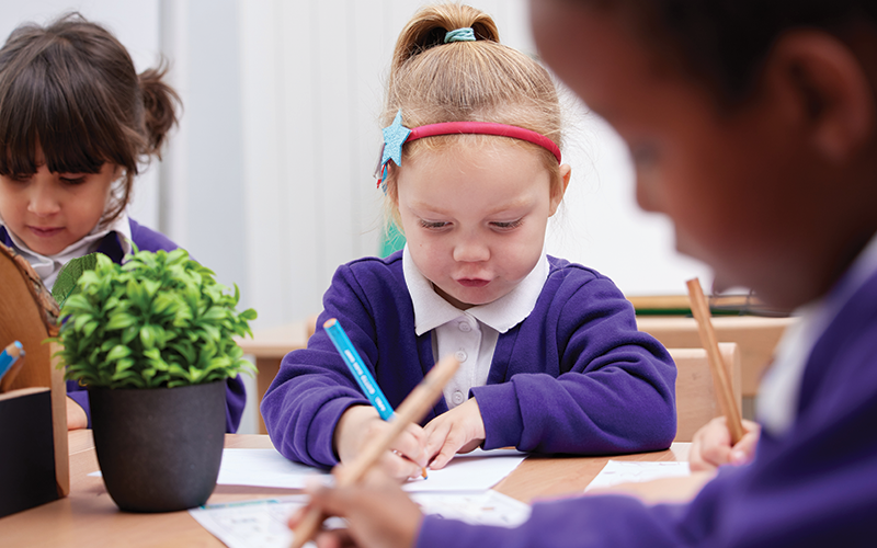 A group of children are sitting at a table writing on a piece of paper.