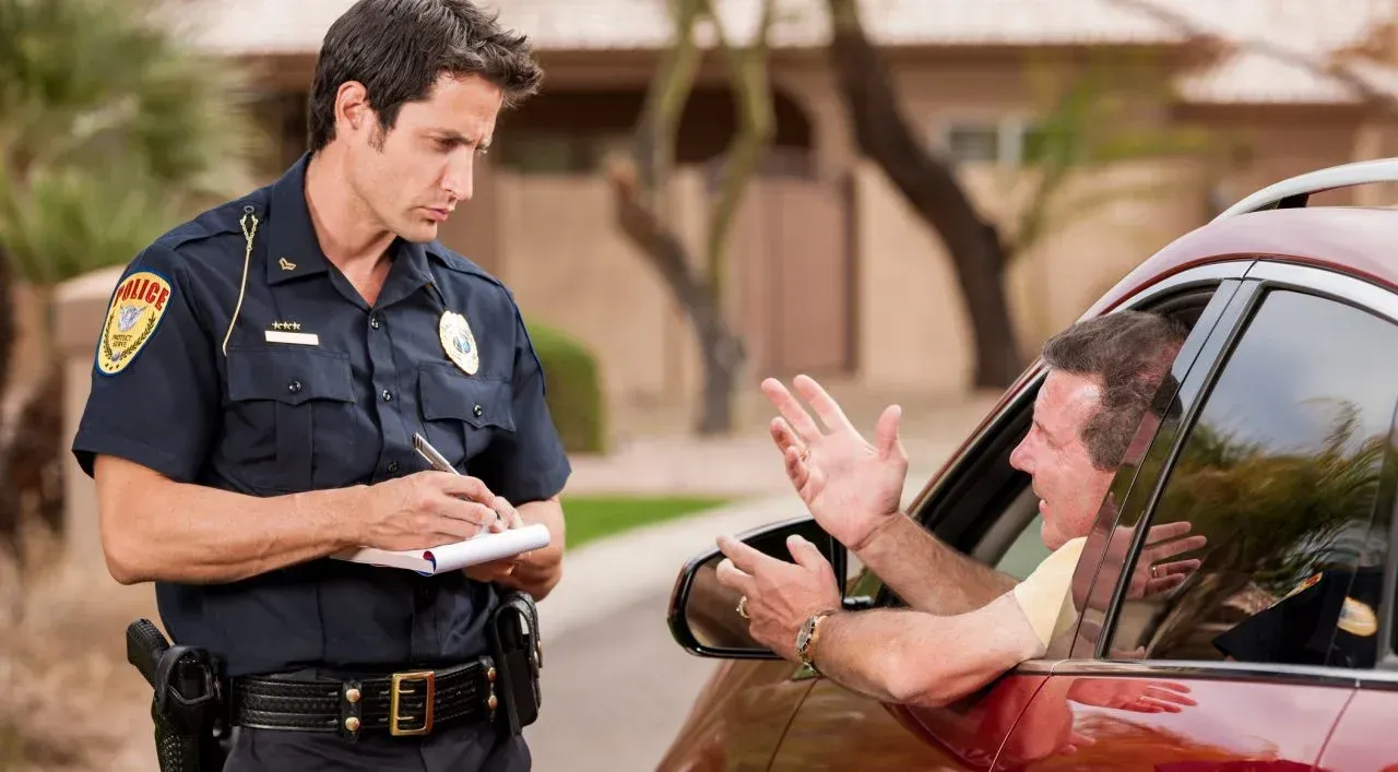 A police officer is writing a ticket to a man in a car.