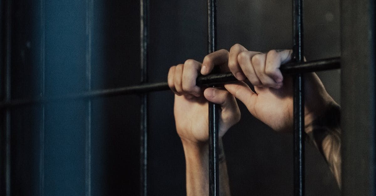 A close up of a person 's hands behind bars in a prison cell.