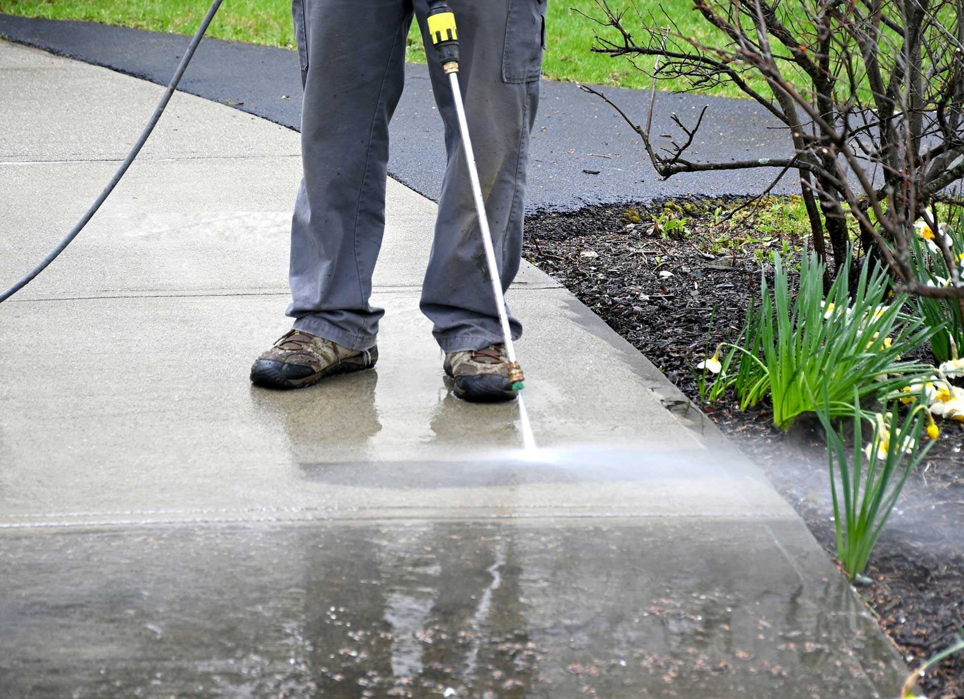 A man is using a high pressure washer to clean a sidewalk