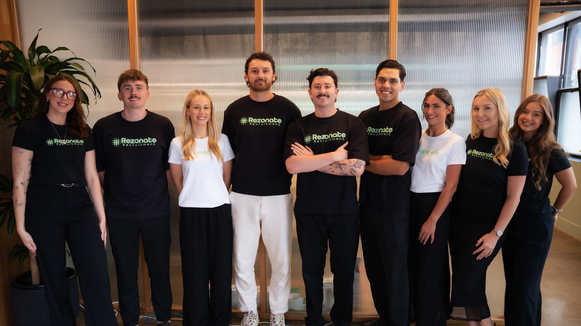 Group of nine people in a modern office, wearing black and white shirts, smiling at the camera.