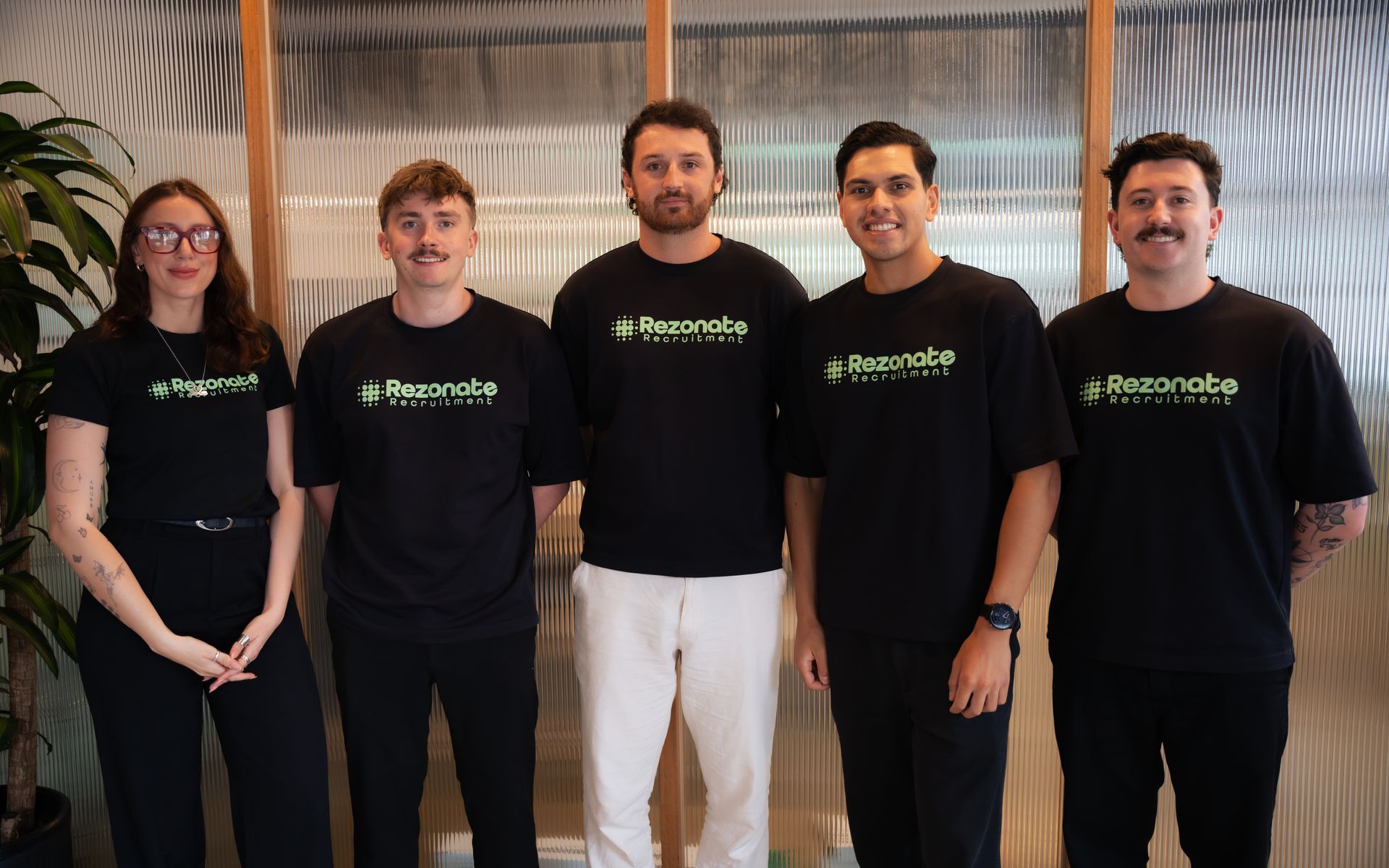 Five colleagues high-fiving. Office setting with stairs, smiling faces, and a sofa.