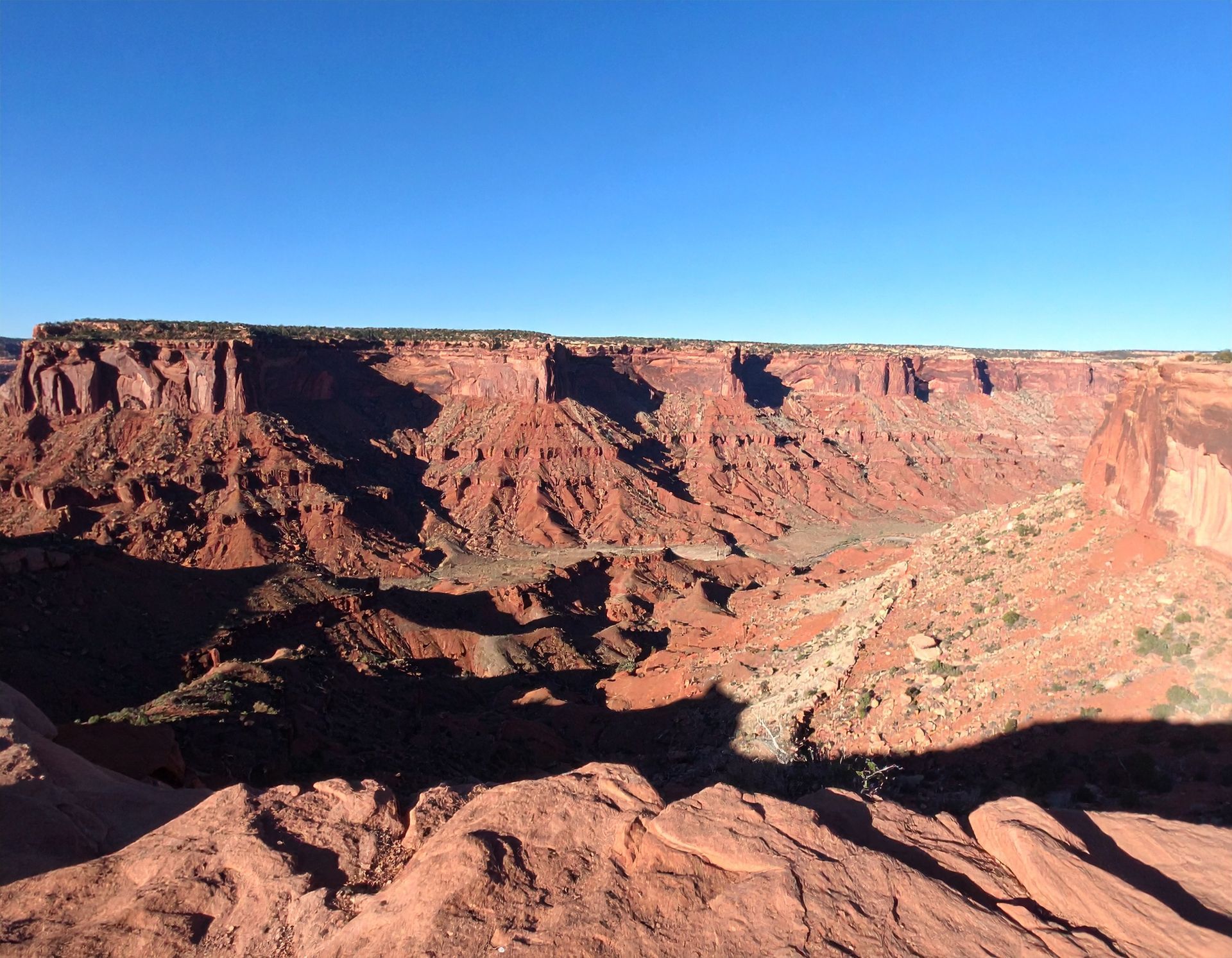 Red sandstone canyon cliffs under a clear blue sky, with deep shadows across the rocky foreground.