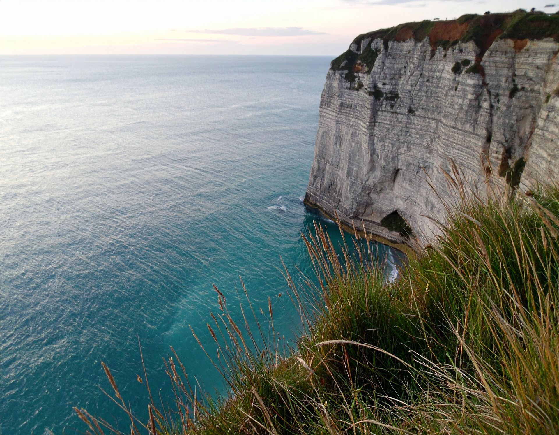 Cliffside overlooking calm blue ocean at sunset, with grassy foreground and white rock face