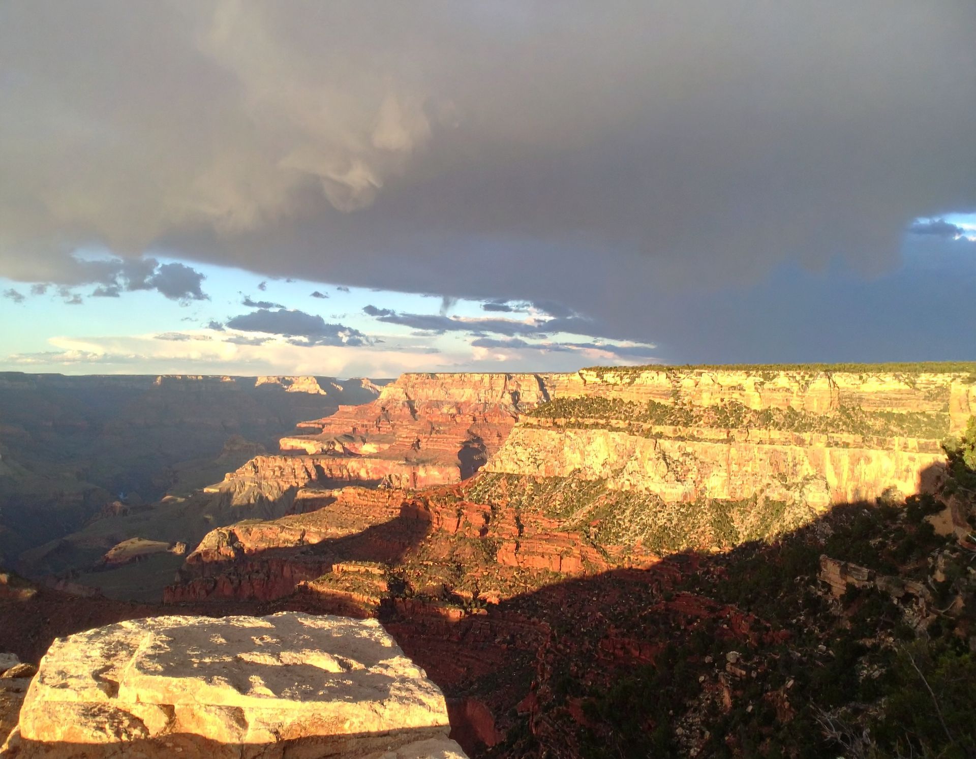 Sunlit Grand Canyon cliffs beneath a dark storm cloud at sunset
