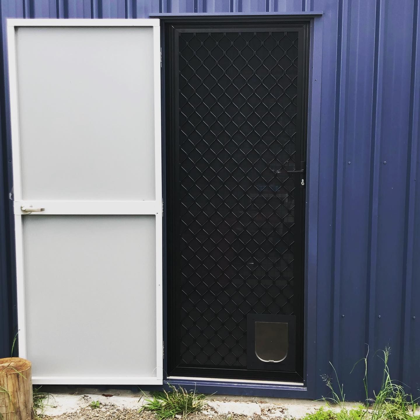 A blue building with a white door and a black door with a cat door. — Browny's Glass & Aluminium in Hallidays Point, NSW