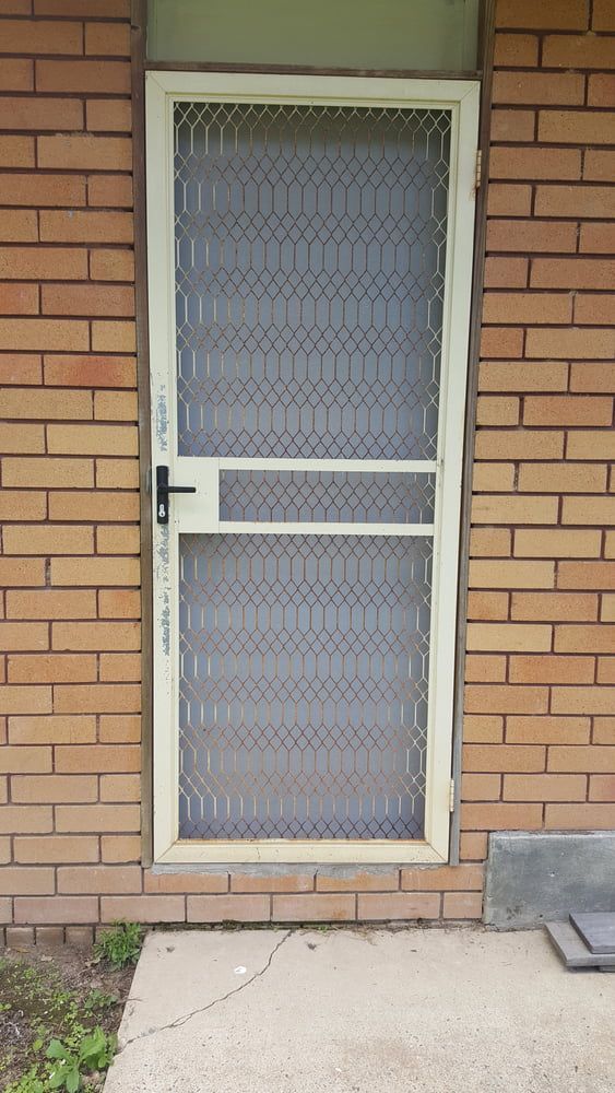 A White Screen Door Is Sitting On A Brick Wall — Browny's Glass & Aluminium in Wingham, NSW